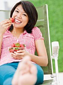 Frau isst Erdbeeren auf einem Gartenstuhl