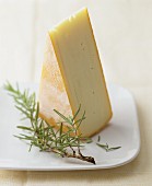 A wedge of Raclette cheese with a sprig of fresh rosemary on a plate