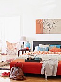 Large double bed below picture with delicate tree motif on wall; breakfast tray with silver teapot and silver-edged bowl on bed