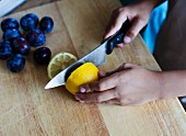 A girl cutting a lemon in half with a knife