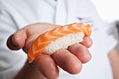 A chef holding a piece of nigiri sushi with salmon