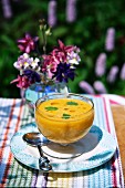 Cold carrot and ginger soup on a table in the garden