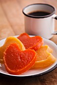 Heart-shaped candies of pumpkin (orange) and sweet potato (yellow) with cup of coffee on the background