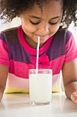 An African-American girl drinking a glass of milk through a straw