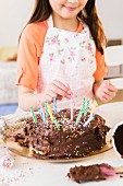 A girl sticking birthday candles into a chocolate cake