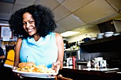 A smiling African-American woman holding a burger on a plate