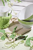 Spring arrangement with felt pea pods on table set with wooden boards, cereal bowls and crocheted teacup cosy
