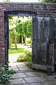 Open wooden door in brick wall showing row of trees in English garden