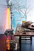 Dining area with accessories in modern hunters' style - thin branches and yellow fluorescent tube in front of landscape poster; bundle of wood and rustic hessian