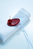 Oriental table decoration; white linen napkin with large, red button and cord as napkin ring