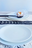 White plate, black spoon with biscuit on doily and printed paper table mat