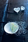 Unconventional decorative idea for wedding banquet - white threads connecting dish with two pear halves and heart-shaped dishes on dark, animal-skin blanket
