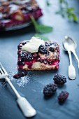 A slice of blackberry cake with cutlery , garnished with cream.