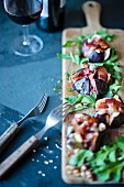 Grilled figs with blue cheese and parma ham on a wooden board with rocket salad.
