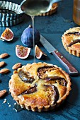 An individual fig and almond tart with honey, fresh figs and a knife.