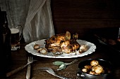 A whole roast chicken on a white plate with garlic, sage, beer and potatoes.