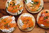 Blinis topped with smoked salmon, sour cream and chives on a wooden board