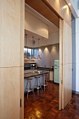 View through open, wooden sliding elements of kitchen counter, pendant lamps, bar stools and fridge