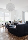 Charcoal sofa on walnut floor and sculptural pendant lamp in minimalist living room