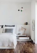 Double bed with white bedspread next to bedside lamp on low table on elegant walnut floor