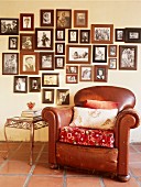 Old, brown leather armchair and side table below collection of framed photos on wall