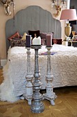 Floor-standing candlestick in front of French bed with wooden headboard next to bedside lamp with pink lampshade