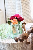 Pinks in preserving jar wrapped in yarn and wooden spindles on upended, rolled wool rug