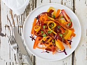 Bright yellow, orange and red carrot salad with micro-greens on a white plate sitting on an antique white wood surface