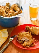 Fried chicken cut open on a red plate with a blue crock full of chicken and a beverage in the background