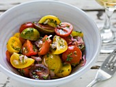 Red, green and yellow heirloom tomato salad with shallots and basil in a white bowl