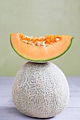 A slice of cantaloupe melon on top of a whole cantaloupe