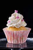 A cupcake decorated with buttercream and pink hearts