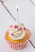 A cupcake decorated with buttercream, pink hearts and a birthday candle