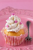 A cupcake decorated with buttercream and pink hearts