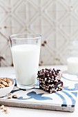 An energy bar with chocolate and nuts next to a glass of milk