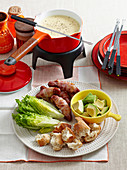 A cheese fondue with breadsticks, avocado, , lettuce and sausages wrapped in bacon