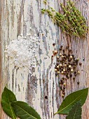 Thyme, bay leaves, peppercorns and coarse salt on a wooden surface