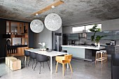 Blick in offenen Designer-Küchen-Essbereich mit puristischem elegantem Holz-Einbauregal als Raumteiler, Betondecke mit zwei Pendel-Kugelleuchten
