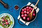 Caramelised radishes in a pan with a plate of feta and peas