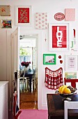 Framed colourful fabric samples and pictures on kitchen wall, fruit bowl on antique wooden table, open door with view of dining area