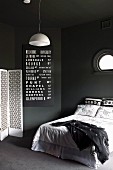 Schwarzer Schlafraum mit weissen Farbakzenten; französisches Bett unter Bullauge, weiße Pendellleuchte und weißer Paravent, schwarze Wandtafel mit weisser Schrift