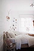 Rustic chair made from birch branches next to double bed with white bed linen in white, wood-clad bedroom