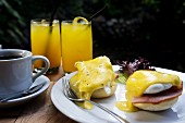 Eggs Benedict with ham served with coffee and juice on a table outside