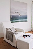 Gemütlicher weißer Hussensessel mit Lese-Stehleuchte und Polstertisch vor ruhigem Meerlandschafts-Gemälde