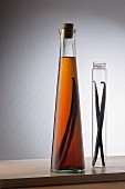 A bottle of vanilla extract and two vanilla pods in a glass tube