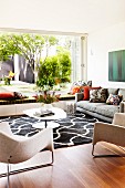 Stylish living room with designer furniture, graphic black and white rug and open terrace window with view into summer garden