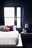 Masculine bedroom with dark blue wallpaper and curtains, white bedlinen and Union flag cushion