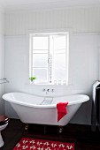 Nostalgische weiße Badewanne vor Sprossenfenster, dunkler Dielenboden und roter Badvorleger