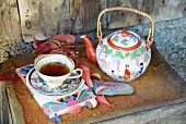 Teatime im Vintagestil vor rustikaler Holzwand, rostiges Tablett dekoriert mit Weinlaub und chinesischer Porzellankanne