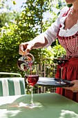 Frau giesst Rotwein in ein Glas am Gartentisch